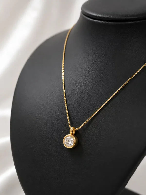 Close-up of round clear solitaire crystal in a gold-tone bezel setting on the Elara delicate pendant necklace