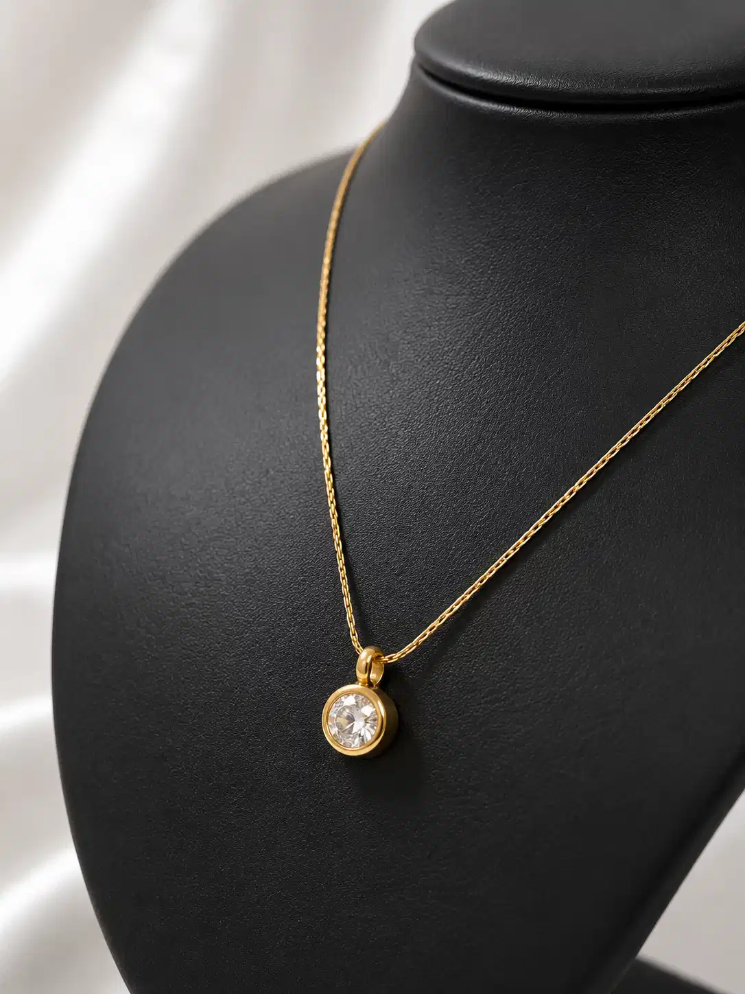 Close-up of round clear solitaire crystal in a gold-tone bezel setting on the Elara delicate pendant necklace