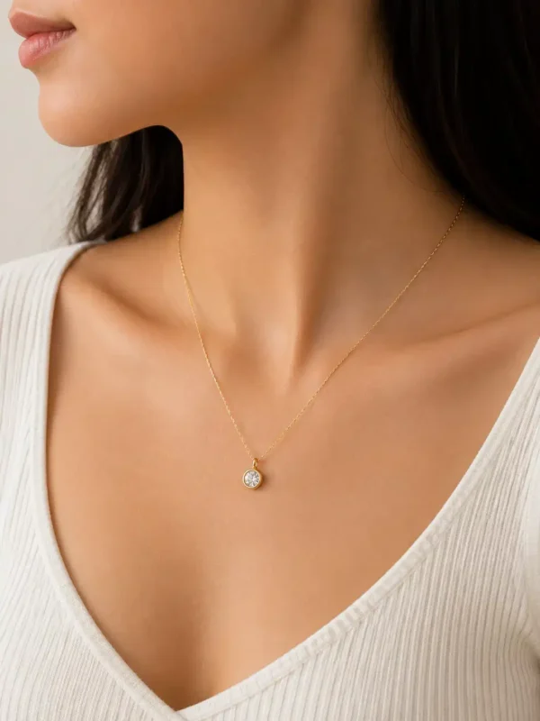 Delicate round solitaire pendant necklace worn with a white V-neck top showing its petite everyday scale