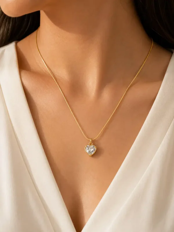 Amora anti tarnish crystal heart necklace in gold tone worn on a woman with a white V-neck outfit