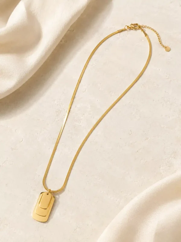 Full flat lay of the Linea gold-tone snake chain necklace with layered rectangular pendant, lobster clasp, extension chain and end tag