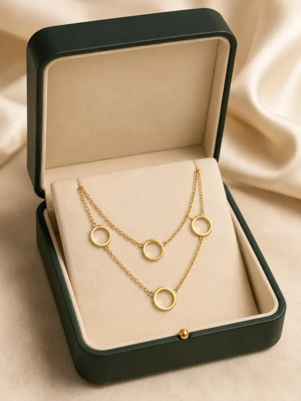 Gold dual-layer open circle necklace arranged inside a dark green and cream jewellery box