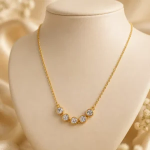 Aurelia gold-toned necklace with five round bezel-set clear crystals displayed on a cream jewellery bust
