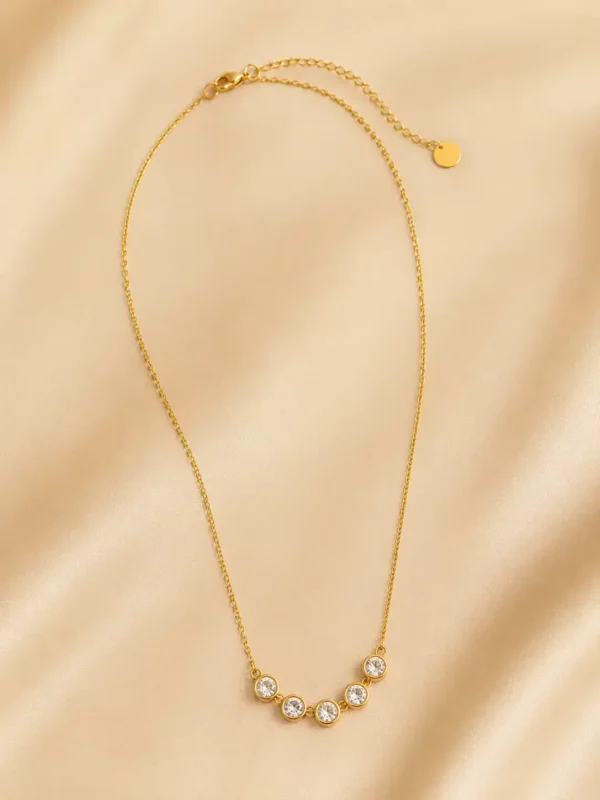 Full Aurelia five-stone crystal necklace laid on champagne satin with lobster clasp and extension chain visible