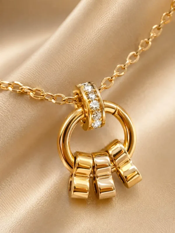 Close-up of gold circular pendant with crystal-set loop and three polished dangling charms