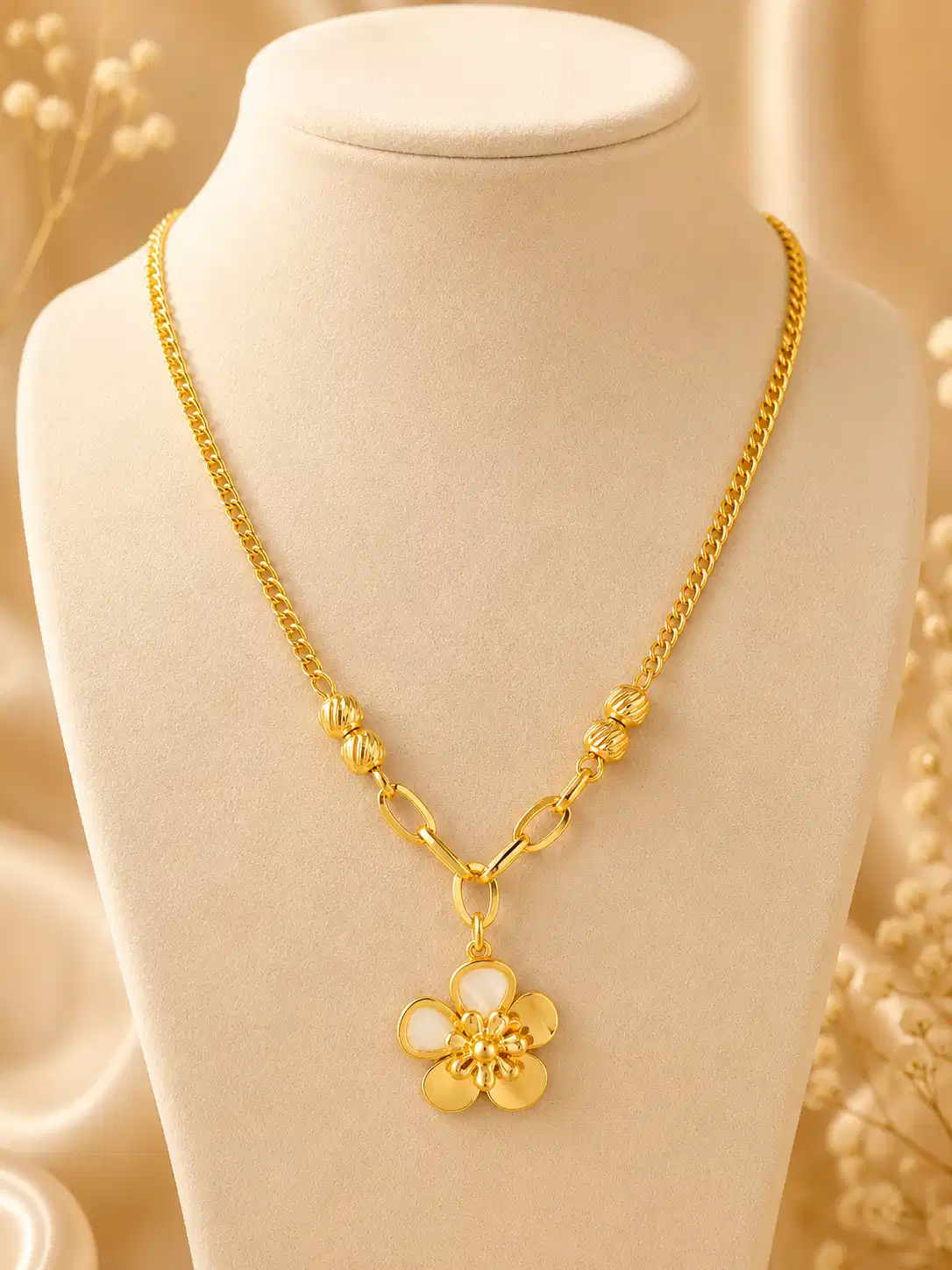 Elara Bloom gold flower pendant necklace displayed on a cream jewellery bust with textured bead and elongated link details