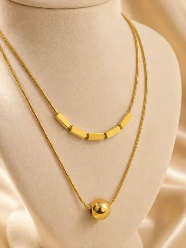 Close-up of gold-tone layered necklace with five rectangular bars and glossy round sphere pendant